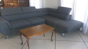 Ein Ecksofa und ein Couchtisch in einem Raum mit Fliesenboden, im Hintergrund ein Essbereich.
