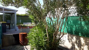 Eine Terrasse mit Glastür, Gartenmöbeln, Blumentöpfen und einem grünen Zaun.