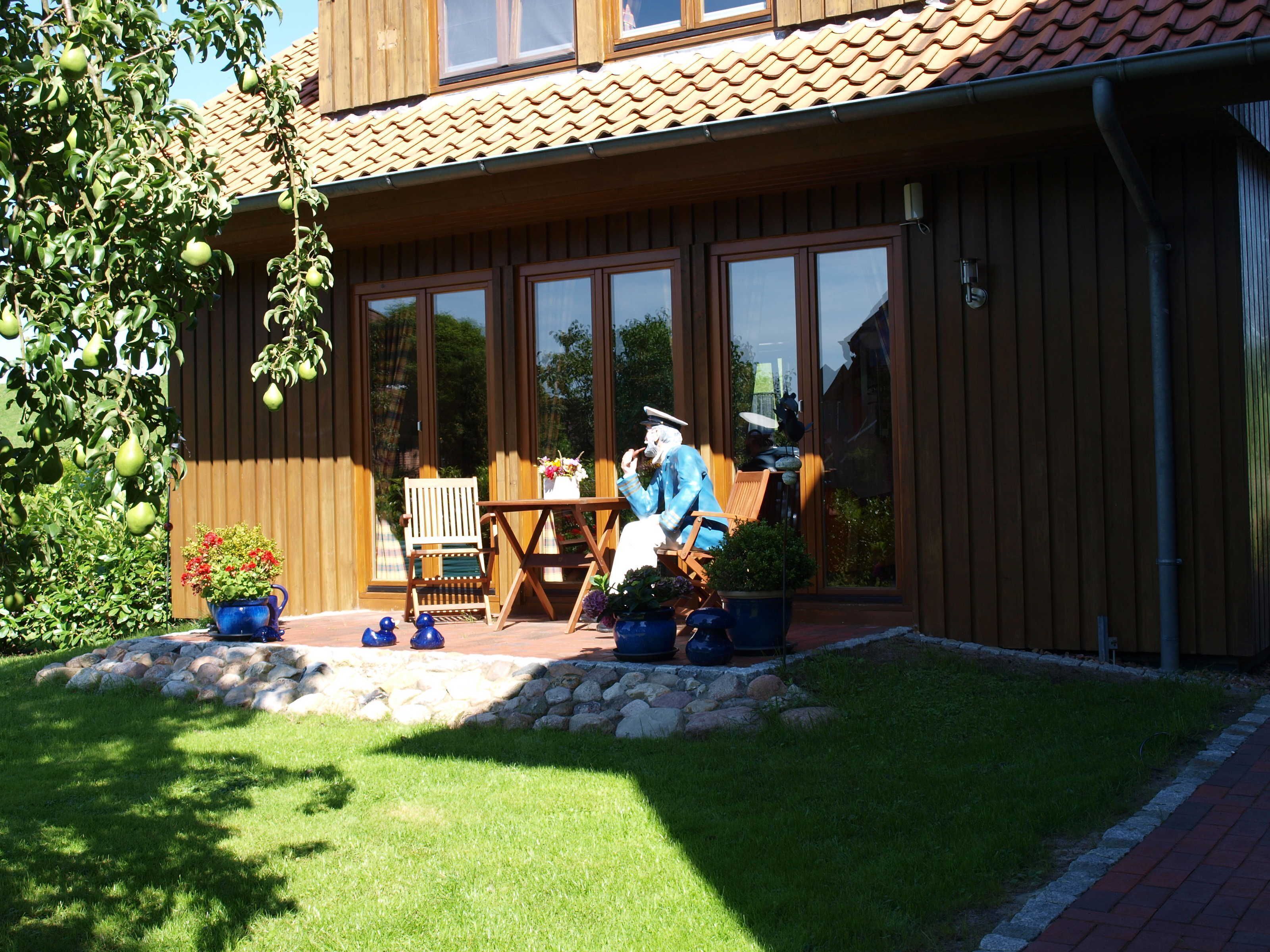 Una casa de madera con techo de tejas, ventanas amplias y un patio con mesa y sillas.