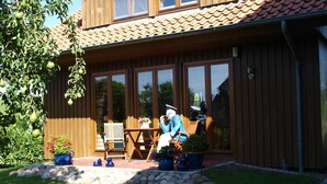 A wooden house with a tiled roof, large windows, and a patio with a table and chairs. - Lütt Hüs, Deutschland (Grünendeich)