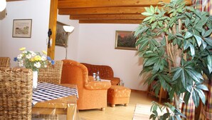 A cozy living room with a wooden ceiling, wicker furniture, and a large plant. - Lütt Hüs, Deutschland (Grünendeich)