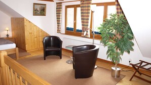 A cozy room with a wooden ceiling, a bed, a black leather chair, a small table, and a potted plant. - Lütt Hüs, Deutschland (Grünendeich)