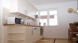 A modern kitchen with white cabinets, a microwave, a stove, and a window with curtains. - Ferienwohung Bootsdeck - Villa Elbdeich (Grünendeich)