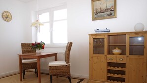 A dining area with a wooden table and chairs, a vase of flowers, a wooden cabinet with wine glasses, and a clock on the wall. - Ferienwohung Bootsdeck - Villa Elbdeich (Grünendeich)