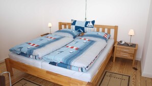 A neatly made bed with a striped blue and white bedding, two bedside tables with lamps, and a wooden floor. - Ferienwohung Bootsdeck - Villa Elbdeich (Grünendeich)
