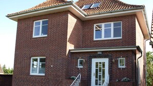 A two-story brick house with a front entrance, a small porch, and a brick pathway leading to the door. - Ferienwohung Bootsdeck - Villa Elbdeich (Grünendeich)