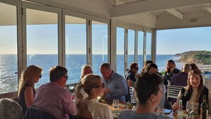 A group of people dining at a table with large windows overlooking the ocean. - Luxury beach stay,  close to the famous SA wine regions (Aldinga)