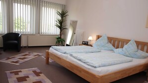 Un dormitorio con una cama de madera, dos almohadas, una mesita de noche con una lámpara, una silla y una planta en maceta.