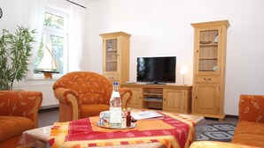Una sala de estar con dos sofás color naranja estampado, un mueble de madera con puertas de vidrio, un televisor y una mesa con mantel rojo y amarillo.