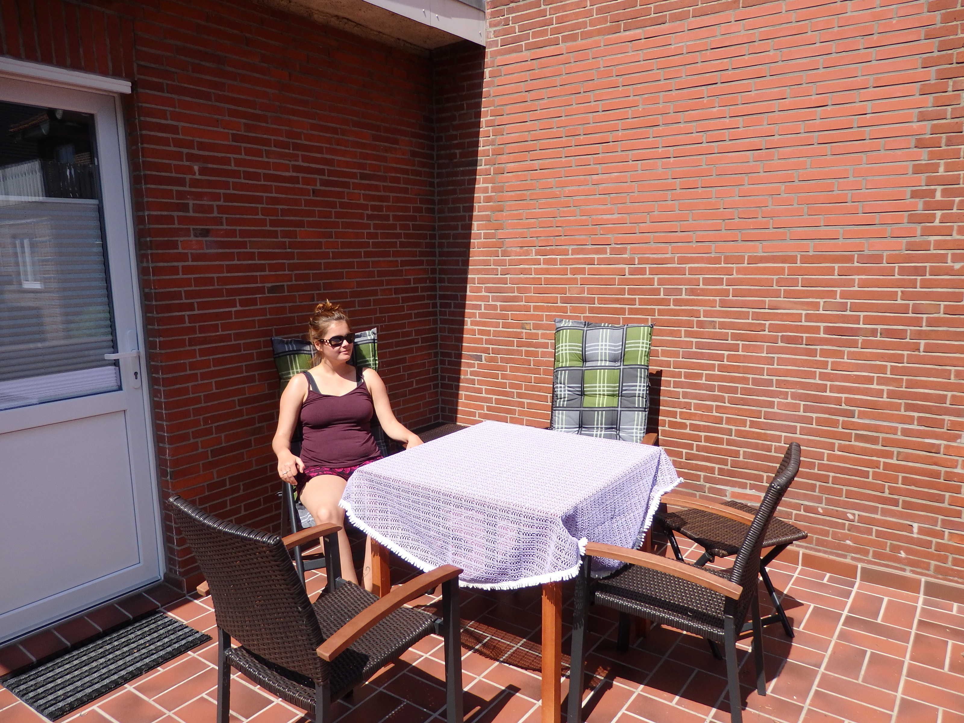 Een terras met een tafel, stoelen, een bakstenen muur en een deur.