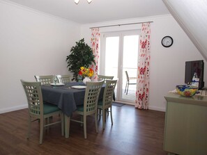 A dining area with a table set for four, surrounded by chairs, a potted plant, and a vase with flowers. - Ferienwohnung Oberland - Haus Helgoland (Grünendeich)