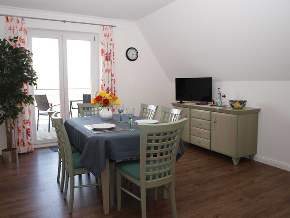 Un coin repas avec une table dressée pour deux personnes, un vase de fleurs et un téléviseur posé sur un meuble.