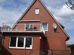 A two-story brick house with a balcony, a satellite dish, and a large window. - Ferienwohnung Oberland - Haus Helgoland (Grünendeich)