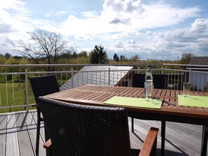 Une terrasse en bois avec une table et des chaises, une bouteille et un verre posés sur la table.