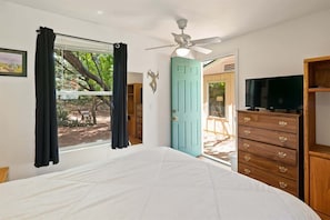 Un dormitorio con cama, ventilador de techo, televisión, cómoda y puerta que da a un espacio exterior.