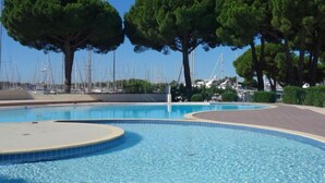 A swimming pool with a curved edge, surrounded by trees and a marina with boats in the background. - Le Grand Galion by Interhome (Port Camargue)