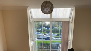 A modern living room with a grey sofa, a black rug, a dining table with chairs, and a large glass door leading to an outdoor area with parked cars and greenery. - 2 Bedroom Ground Floor Riverside Apartment St Neots (Saint Neots)