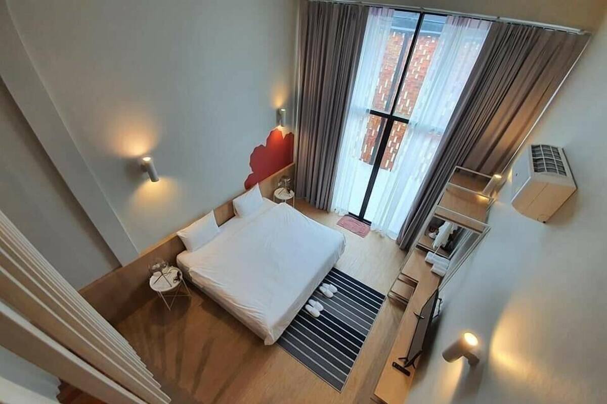 Habitación de hotel con cama, una mesita, una silla, una ventana con cortinas y un equipo de aire acondicionado.