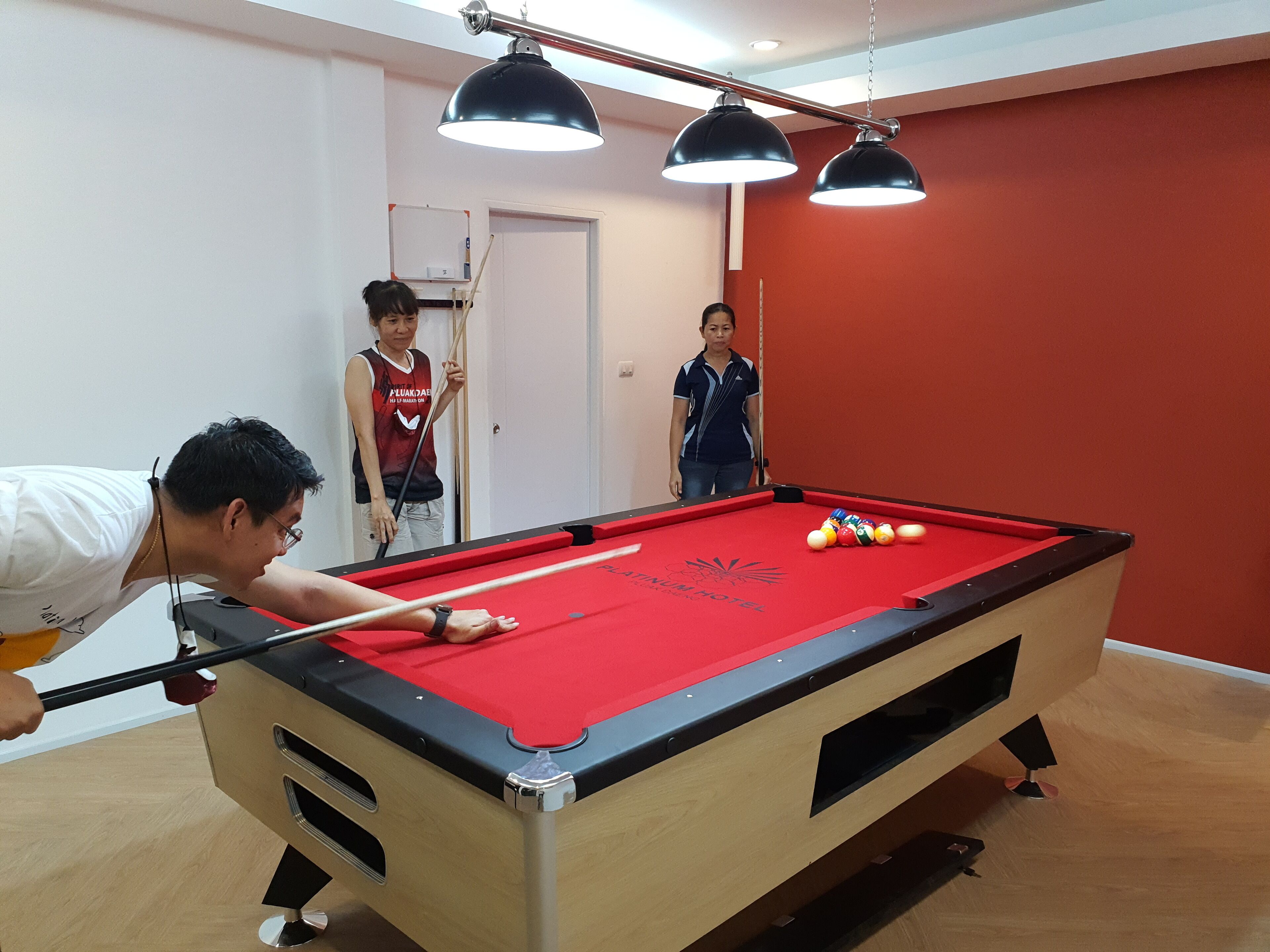 A pool table with a red felt surface, surrounded by wooden walls and a red accent wall.