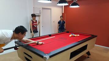 A pool table with a red felt surface, surrounded by wooden walls and a red accent wall.