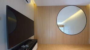 Una habitación moderna con televisión de pantalla plana sobre un soporte negro, un espejo redondo en la pared y suelo de madera.