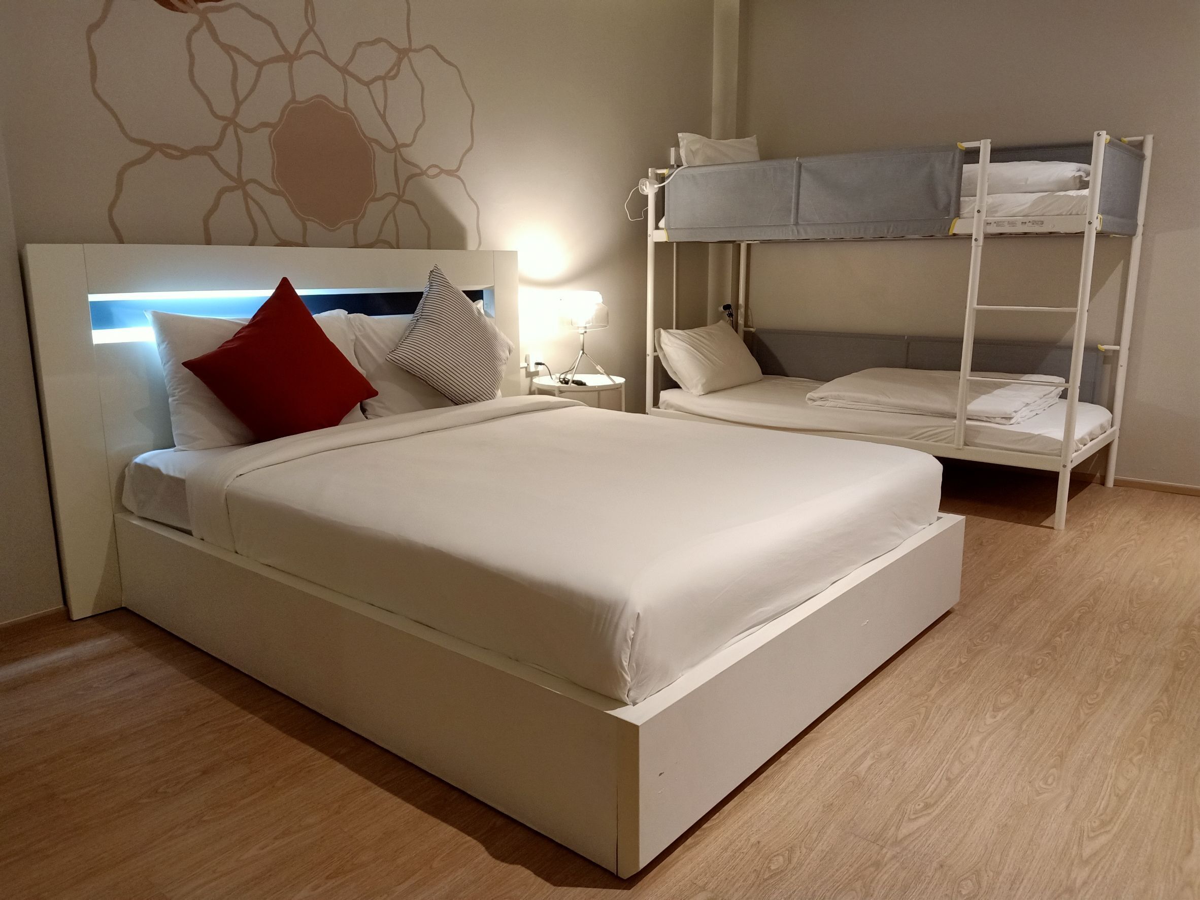 A hotel room with a large bed, a bunk bed, a bedside table with a lamp, and a wall with a decorative pattern.