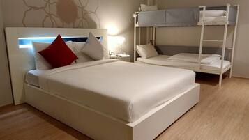 A hotel room with a large bed, a bunk bed, a bedside table with a lamp, and a wall with a decorative pattern.