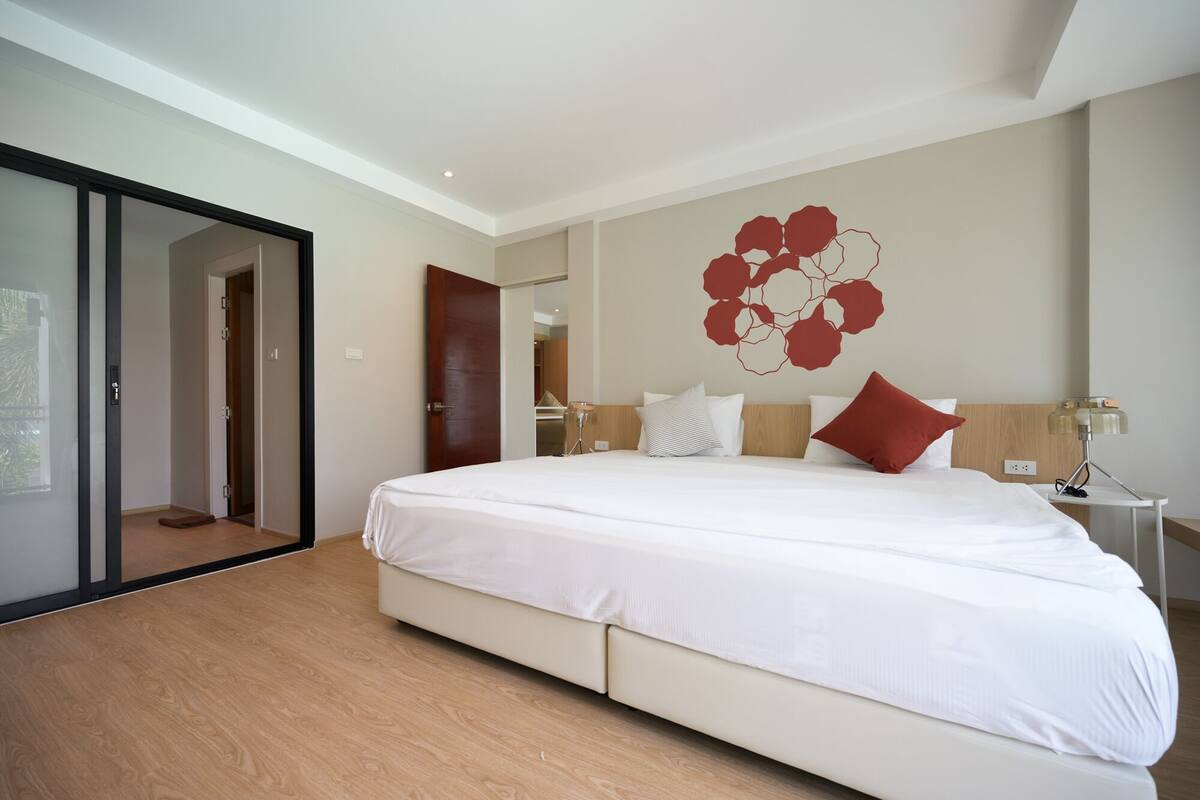 Un dormitorio moderno con una cama grande, piso de madera, una obra de arte abstracta colgada en la pared y un ventanal corredero.