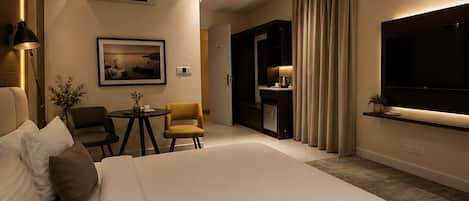 Habitación de hotel con una cama grande, ventilador de techo, televisor montado en la pared y una pequeña mesa con sillas.