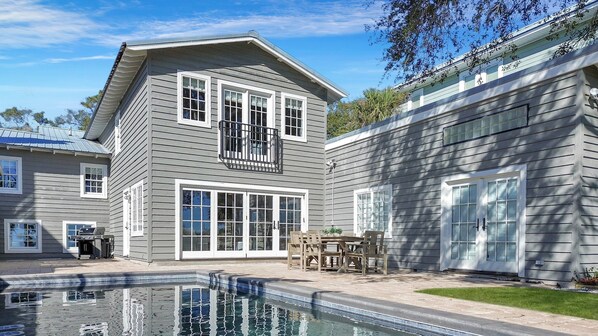 A two-story house with a swimming pool, large windows, and a balcony.