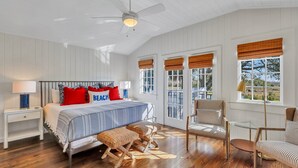 Ein Schlafzimmer mit einem Bett, zwei Stühlen, einem Nachttisch und einem Fenster mit Jalousien.