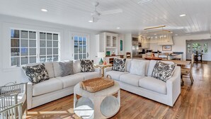 Ein geräumiges Wohnzimmer mit zwei weißen Sofas, einem runden Couchtisch und einem Deckenventilator.