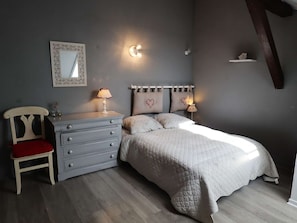 Quarto com cama, penteadeira, cadeira, espelho e arandelas na parede.