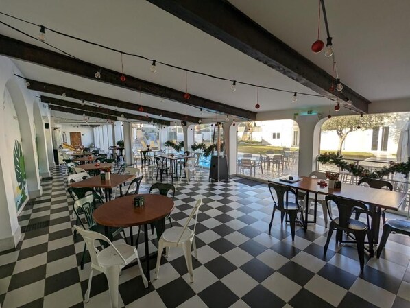 A cafe with checkered flooring, tables, chairs, and hanging light bulbs.