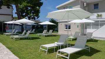 Area piscina con lettini e ombrelloni, un vialetto in pietra e un edificio con tetto piatto.