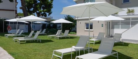 A poolside area with lounge chairs and umbrellas, a stone pathway, and a building with a flat roof.