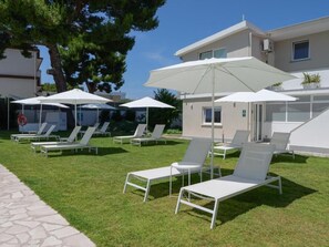 Un espace aménagé au bord de la piscine, avec des chaises longues et des parasols, un chemin en pierre et un bâtiment doté d’un toit plat.