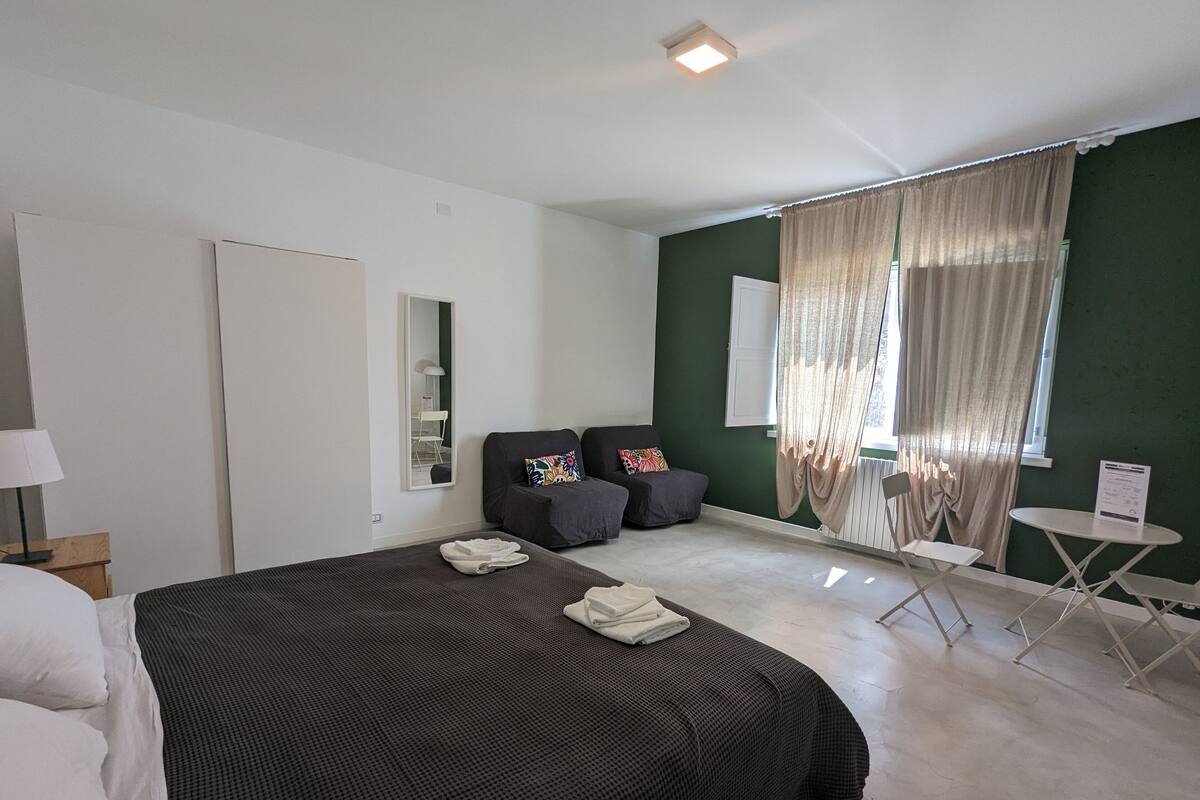 Une chambre moderne avec un grand lit, un petit canapé, une table d’appoint et une fenêtre avec des rideaux.
