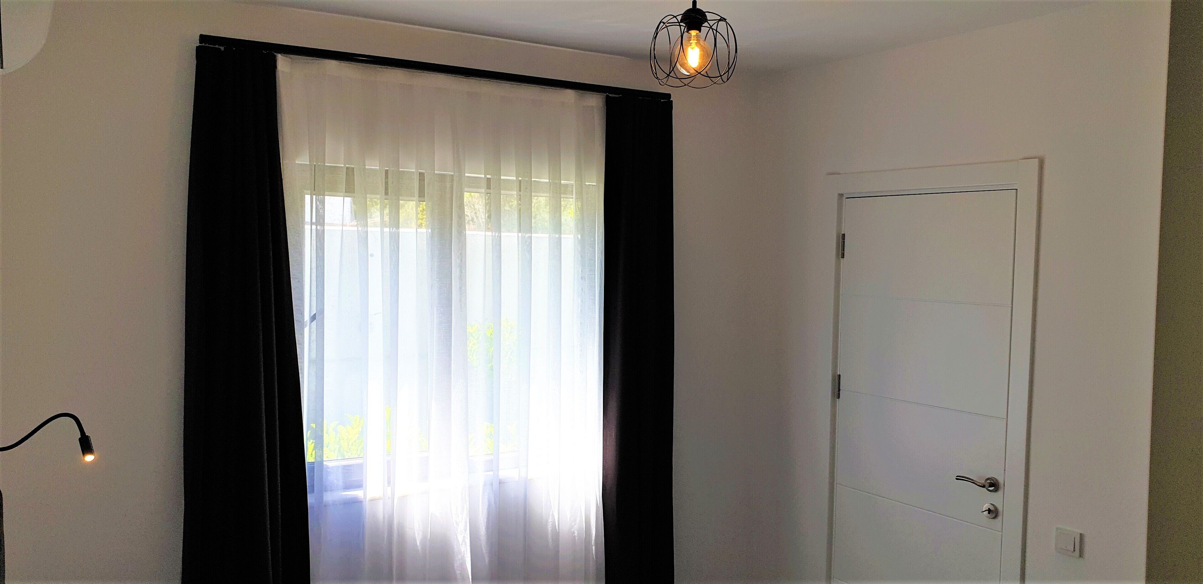 Une pièce avec une porte, un luminaire et des rideaux légers.