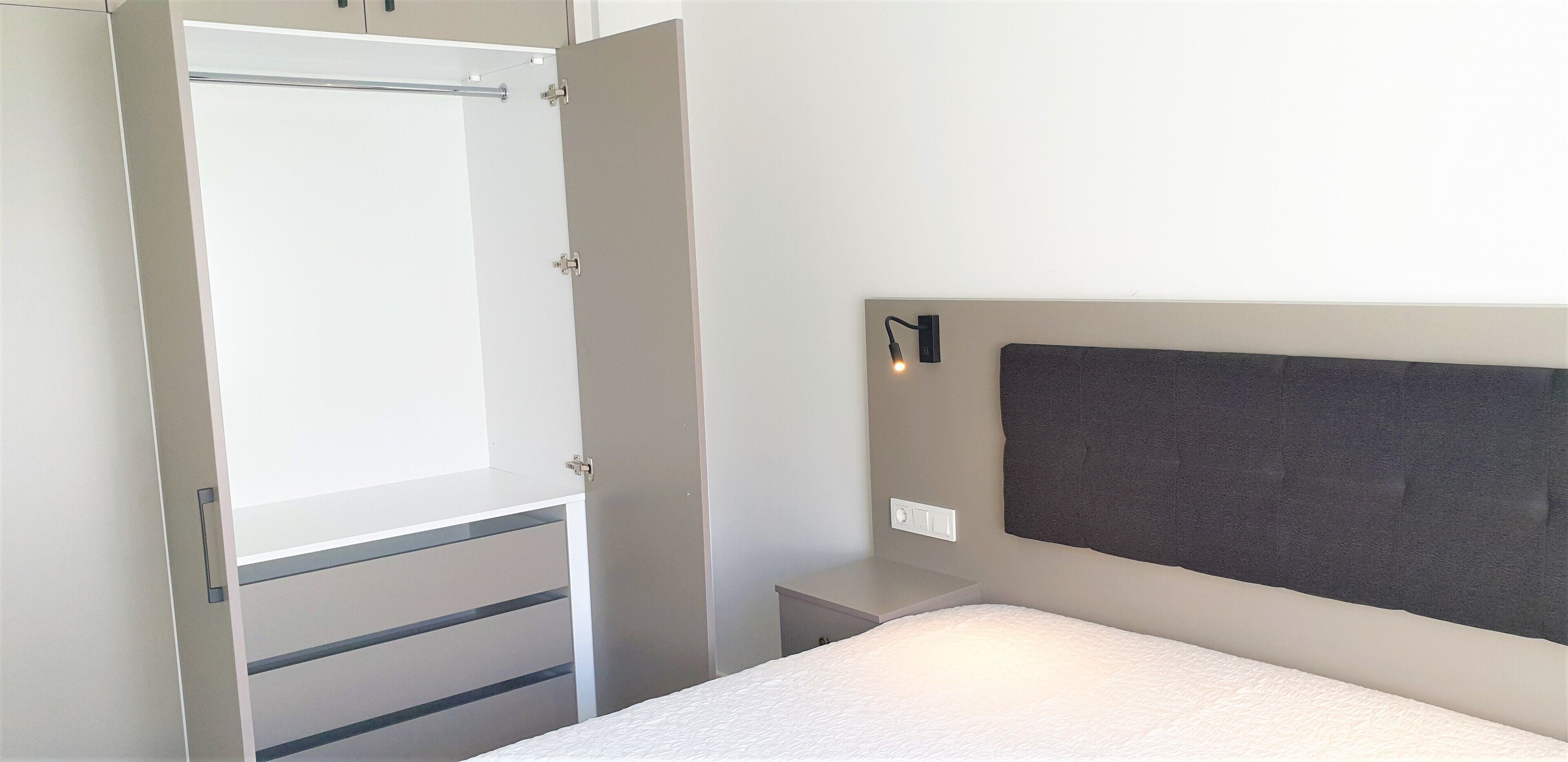 A bedroom with a bed, a bedside table, a nightstand, a wall-mounted light, and a wardrobe with a sliding door.