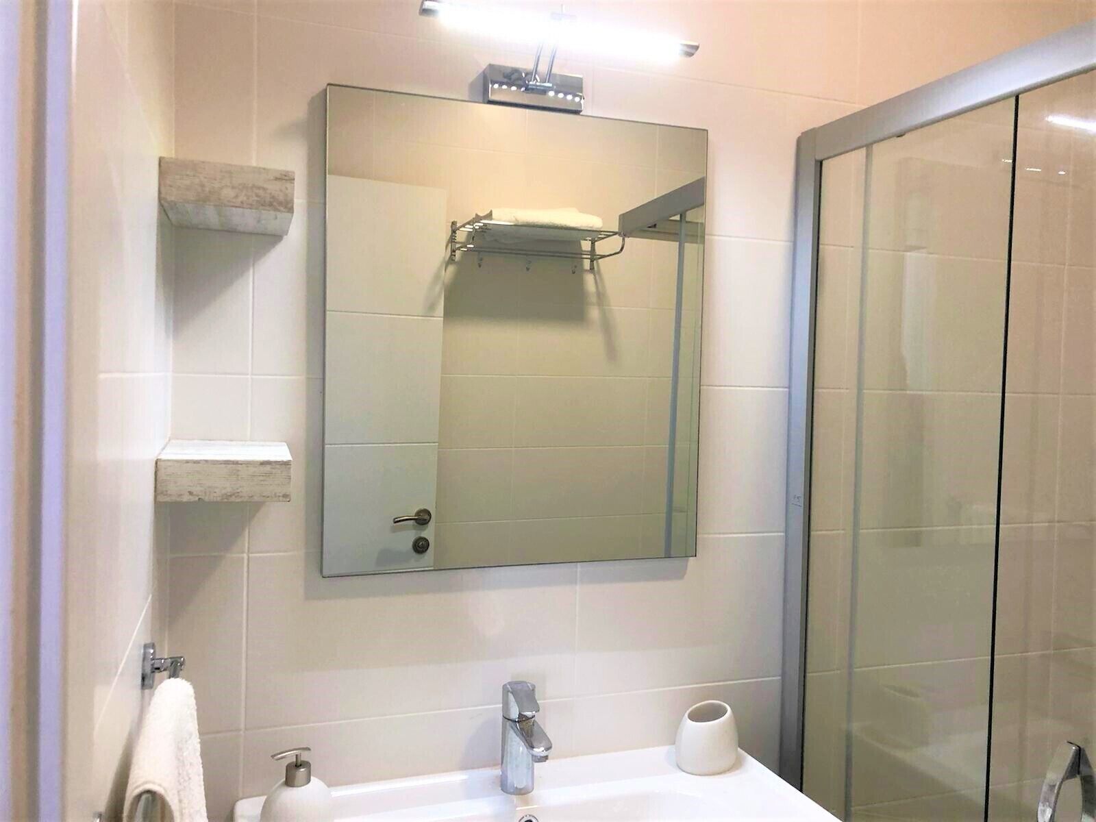 A modern bathroom with a large mirror, a sink, a glass shower enclosure, and a towel rack.