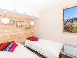 A bedroom with two beds, wooden panel walls, white bedding, and a window with a mountain view.