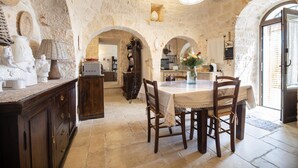 Un interior rústico de piedra con comedor que incluye una mesa, sillas, armarios de madera y una araña.