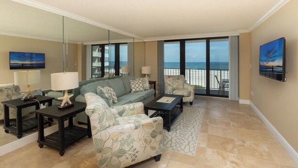 A spacious living room with a large window overlooking the beach, a sofa, a coffee table, and a TV.