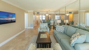 A spacious living room with a large sofa, a coffee table, and a dining area with chairs and a table.