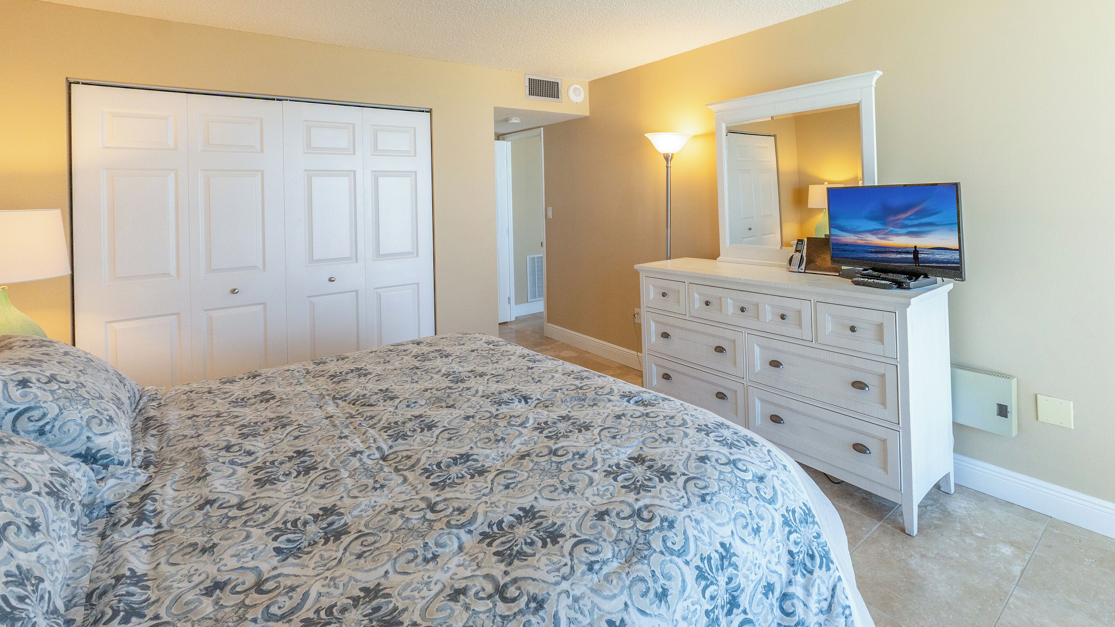 A bedroom with a large bed, a dresser, a TV, and a door.