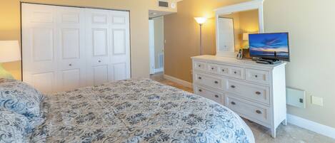 A bedroom with a large bed, a dresser, a TV, and a door.
