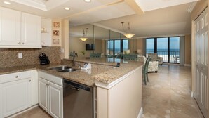 A kitchen with granite countertops, stainless steel appliances, and white cabinetry. There is a dining area with a view of the ocean.