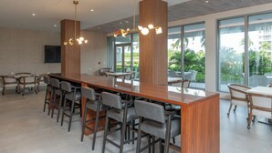 A modern conference room with a long wooden table, grey chairs, and a large window offering a view of palm trees.