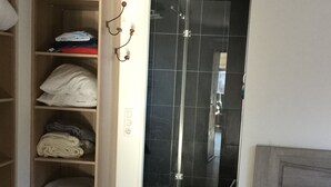 Ein Hotelzimmer mit begehbarem Kleiderschrank, einer Dusche mit schwarzen Fliesen und einem Bett mit weißer Bettwäsche.